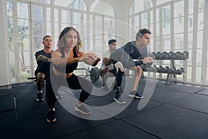 Group of determined multiracial young adults in sports clothing doing squats at the gym