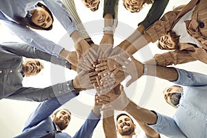 Group of different people stand in a circle and fold their arms together as a symbol of cooperation.