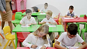 Group of diligent schoolkids drawing with cheerful female teacher at classroom