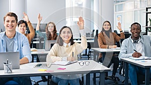 Portrait of diverse students raising hands at classroom