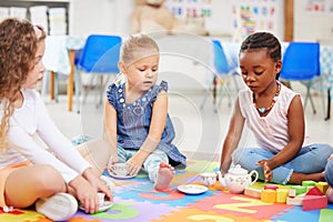 Group of diverse adorable little girls sitting cross legged on the floor in preschool and having a tea party. Three cute