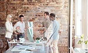 Group of diverse architects discussing plans, blueprints and schematics during a meeting in their office boardroom