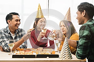 Group of diverse Asian friends gather to celebrate Christmas with champagne and eating pizza at home. Joy of holiday