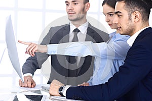 Group of diverse business people discussing questions at meeting in modern office. Colleagues working with computer at