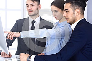 Group of diverse business people discussing questions at meeting in modern office. Colleagues working with computer at