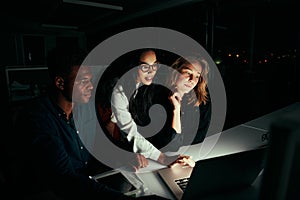 Group of diverse business people working overtime in dark office using laptop