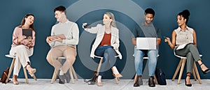 Group of diverse businesspeople sitting on chairs in a row in an office together. Five business professionals sitting