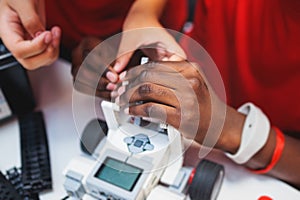 Group of diverse children kids with robotic vehicle model, close-up view on hands, science and engineering lesson in a classroom,