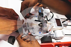 Group of diverse children kids with robotic vehicle model, close-up view on hands, science and engineering lesson in a classroom,