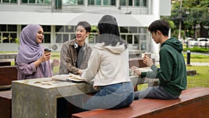 A group of diverse college students is discussing and working on a group project in a campus park