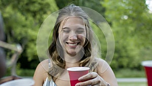 A group of diverse friends say cheers in a park while having a bbq.