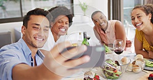 Group of diverse male and female friends taking selfie at dinner party on patio