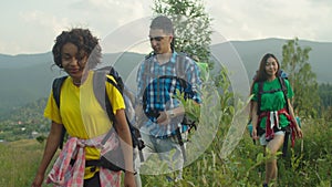 Group of diverse multiracial hikers with backpacks enjoying mountain hiking at sundown