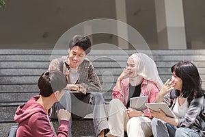 A group of diverse, multiracial young Asian university students are seen resting and chatting outdoors sitting on steps