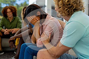 Group of diverse people sitting on sofa, talking and crying in group therapy session