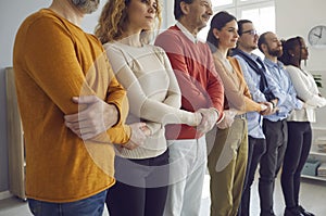 Group of diverse people standing in row and holding hands as concept of community support