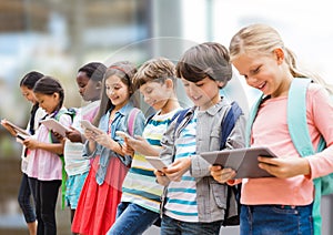 Group of diverse school students using electronic devices against blurred background