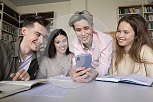 Group of diverse schoolmates using smartphone in library