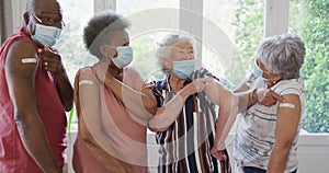 Group of diverse senior people wearing face masks showing their vaccinated shoulders at home