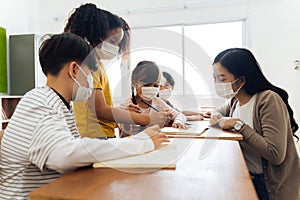 Group of diverse students in school building discussing in group study class. Elementary pupils are wearing a face mask