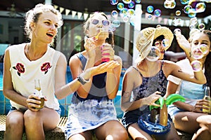 Group of diverse women sitting by the pool blow soap bubble