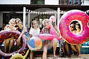 Group of diverse women sitting by the pool with inflatable tubes