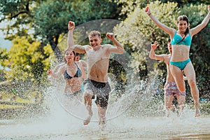 A group of diverse young people having fun together as they run along the river and play water games