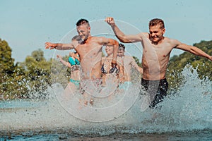A group of diverse young people having fun together as they run along the river and play water games