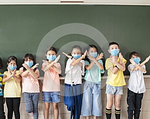 Group of diverse young students wear mask and showing stop sign gesture in classroom