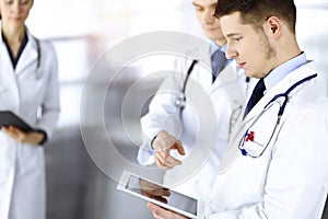 Group of doctors are checking medical names on a computer tablet, with a nurse with a clipboard on the background