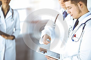 Group of doctors are checking medical names on a computer tablet, with a nurse with a clipboard on the background, while