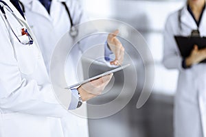 Group of doctors are checking medical names on the computer tablet, when a nurse with a clipboard is making some notes