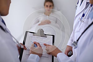 A group of doctors discussing medical history close up , a happy smiling patient in the background.