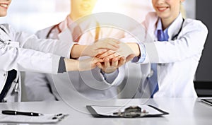 Group of doctors joining hands as a circle and ready to help patients while sitting at the desk in modern hospital