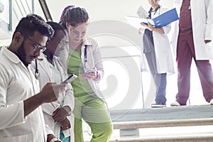 A group of doctors on the steps in the hospital. Young people of mixed race, in medical clothes, examine X-rays, use a smartphone