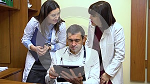 A group of doctors talking. Two women and a man. Male doctor keep a tablet.