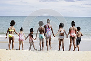 Group of eight boys and girls holding hands in a line running to sea water, cute kids having fun on sandy summer beach, happy