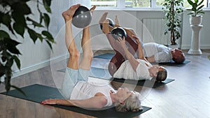 Group of elderly people practice pilates with soft ball in studio