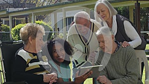 Group of elderly retired people in the garden smiling using tablet - Active seniors outdoor