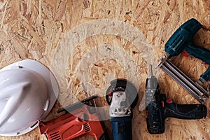 Group of electric hand tools jigsaw, grinder, drill, nail gun and white safety helmet on wooden background