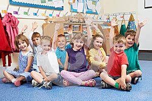 Group Of Elementary School Pupils Putting Hands Up In Class