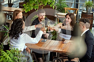 Group of employees, colleagues meeting at cafe after work, celebrating successful deal, drinking champagne and cocktails