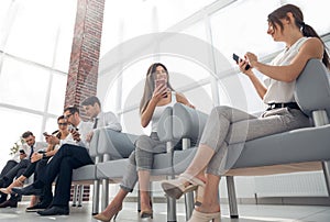 Group of employees with gadgets sitting in the office hallway