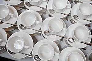 A group of empty white cups and saucers with a teaspoon