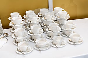 group of empty white cups and saucers with a teaspoon. Many rows of white cups of tea, standing on top of each other, for serving