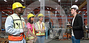 Group of engineer in safety vest meeting with young manager in black suit in an industrial or factory setting. Everyone wearing