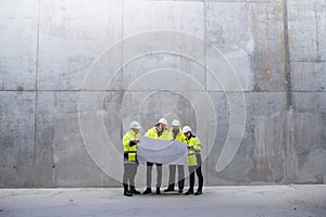 A group of engineers standing against concrete wall on construction site.