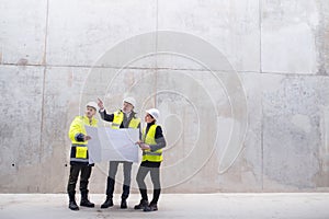 A group of engineers standing against concrete wall on construction site.