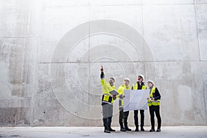 A group of engineers standing against concrete wall on construction site.