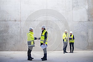 A group of engineers standing on construction site, shaking hands.